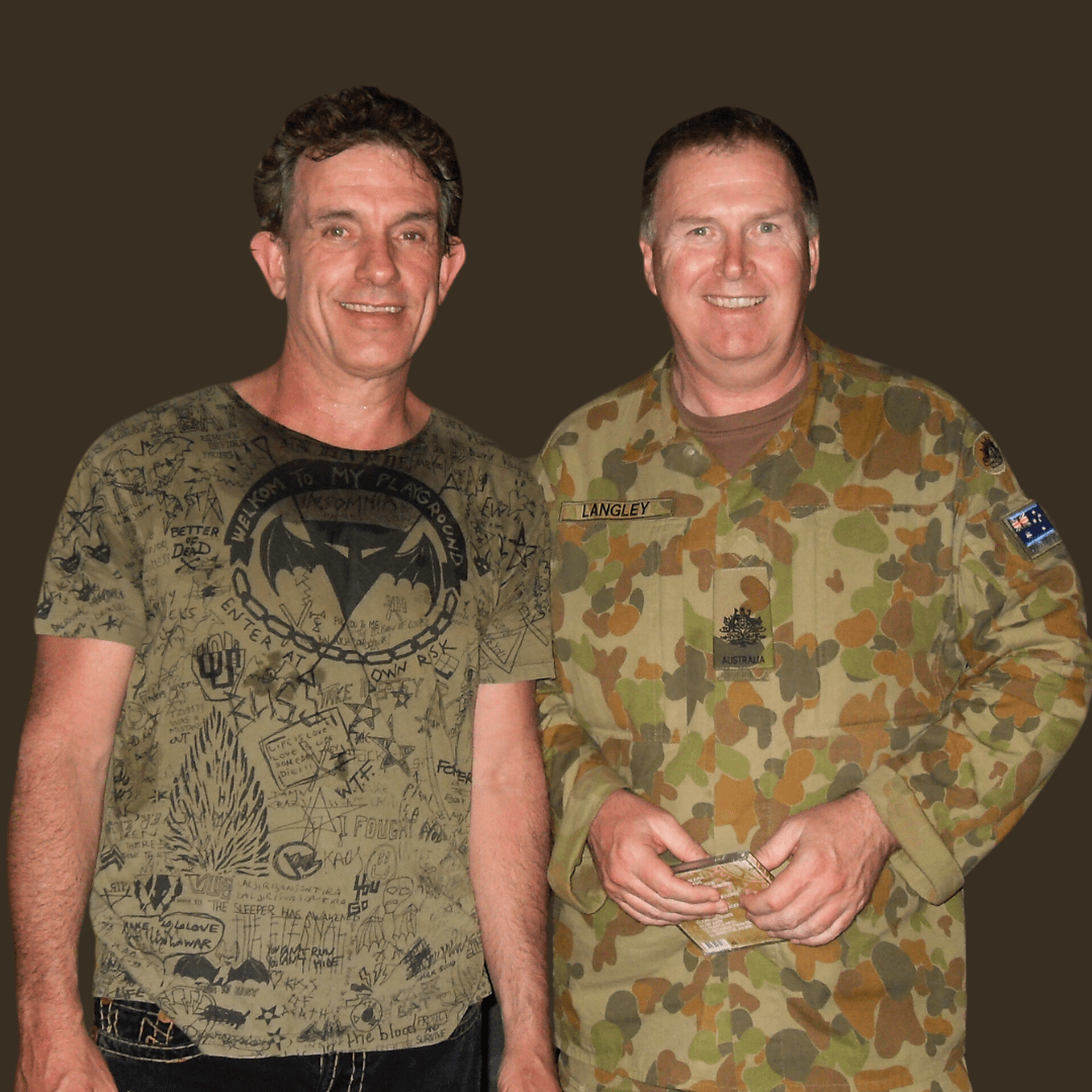 Cold Chisel's Ian Moss with WO1 Mark Langley in East Timor. Cold Chisel's Ian Moss with WO1 Mark Langley in East Timor. Ian Moss is wearing a green t-short with black detail and Mark is wearing his Army camouflage. They are standing close together and smiling at the camera.