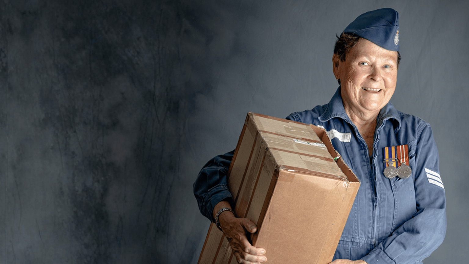 A veteran wears her medals and old uniform, carrying a box. 