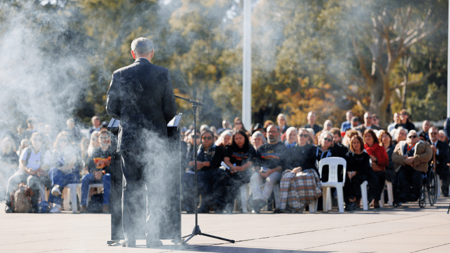 Speaker at lectern facing a crowd with smoke moving across the photo.