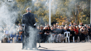 Speaker at lectern facing a crowd with smoke moving across the photo.