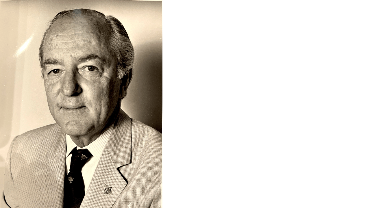 Black and white portrait of an older man in a suit, photographed from the chest up.