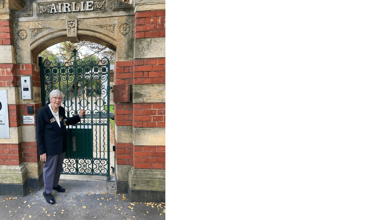 Elizabeth Mackenzie standing in front of an iron gate and decorative tall brick fence, the gate reads 'Airlie'.