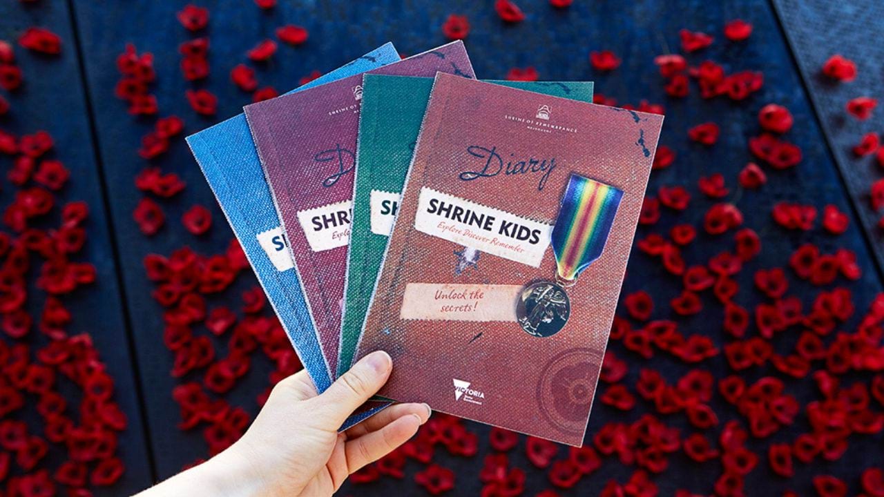 Four booklets being held up against a poppy clad wall.