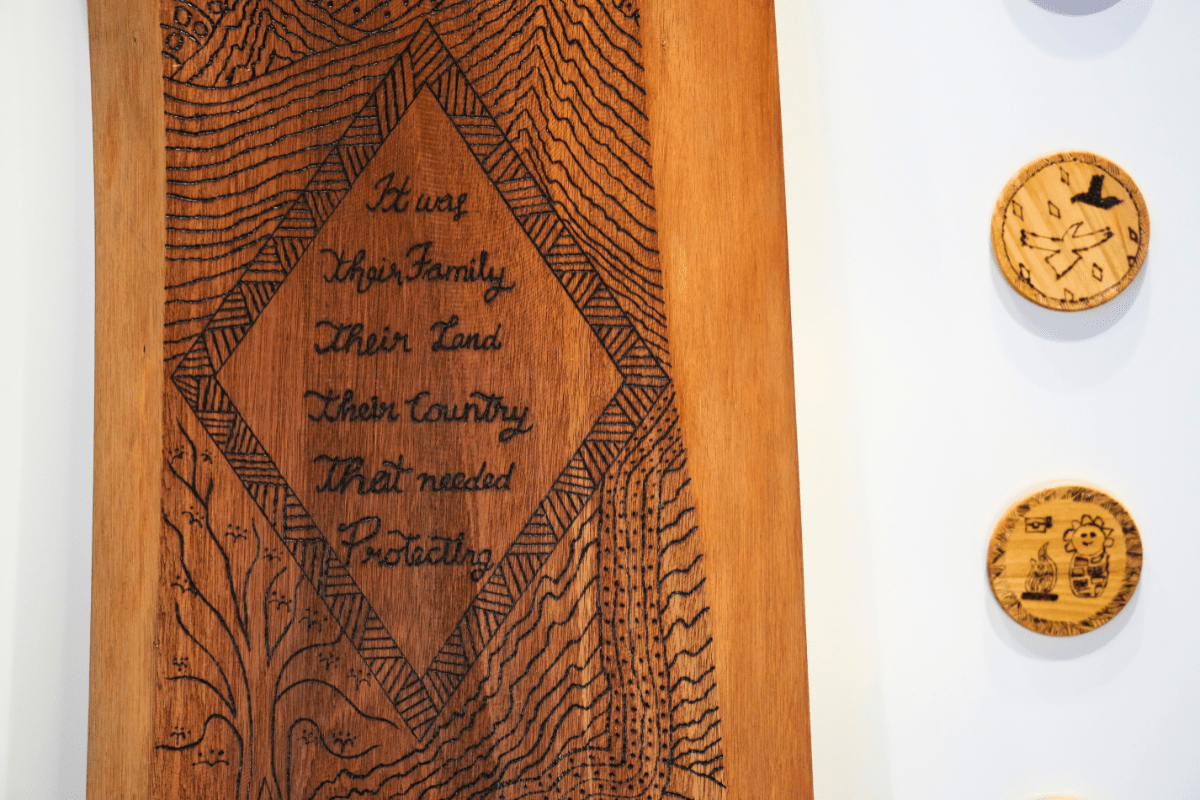 Wood carving with text in a diamond shape: It was their family, their land, their country that needed protecting. Decorative lines are carved around the text.