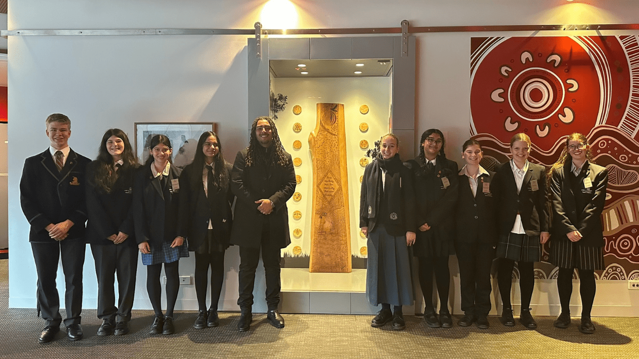 A group of students and an instructor in front of a timber artwork in a display case